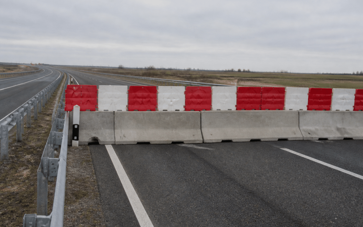 O imagine care prezintă un segment de autostradă blocat transversal de bariere din beton peste care sunt așezate elemente de plastic în culorile roșu și alb