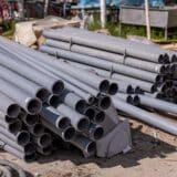 O stivă de țevi de plastic gri pentru canalizare sau alimentare cu apă depozitate pe un șantier