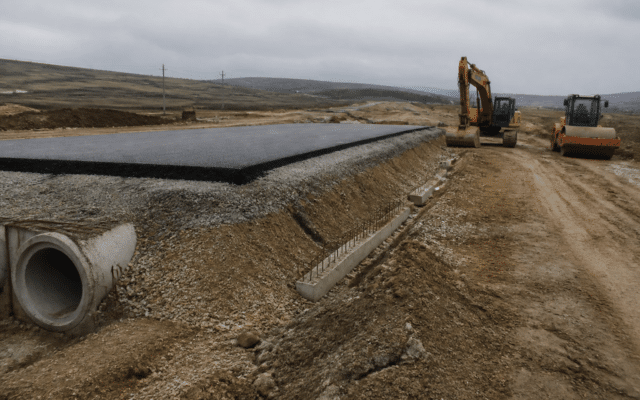 Un șantier de infrastructură rutieră într-o zonă deluroasă, sub un cer înnorat