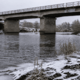 O imagine de iarnă arătând un pod masiv de beton peste un râu