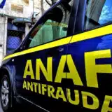 O masina de culoare albastra cu insemnele ANAF Antifrauda parcata in fata unei cladiri pe care se afla o placuta cu sigla ANAF