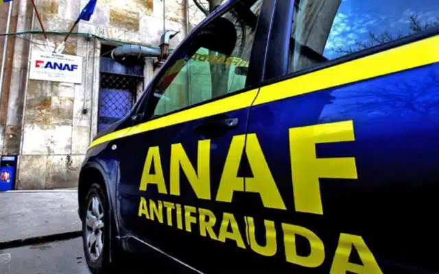 O masina de culoare albastra cu insemnele ANAF Antifrauda parcata in fata unei cladiri pe care se afla o placuta cu sigla ANAF