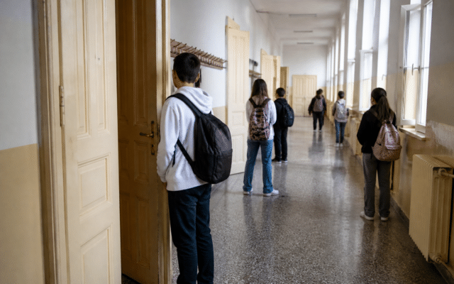 Un hol lung de școală, cu uși înalte din lemn pe partea stângă și ferestre pe partea dreaptă
