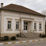 O clădire administrativă sau publică, cu un singur etaj, având fațada albă, coloane la intrare și o scară de acces