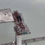Vedere de sus a unui pod aflat în plină construcție, întrerupt deasupra unei ape