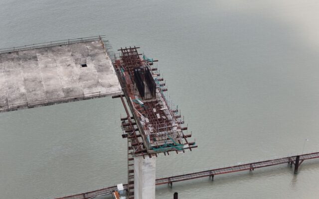 Vedere de sus a unui pod aflat în plină construcție, întrerupt deasupra unei ape