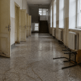 Un coridor lung și pustiu de școală, cu uși deschise pe partea stângă și ferestre pe partea dreaptă