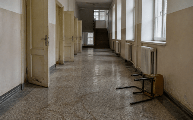 Un coridor lung și pustiu de școală, cu uși deschise pe partea stângă și ferestre pe partea dreaptă