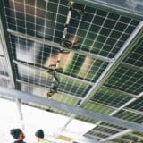 O vedere de sub un sistem de panouri fotovoltaice montate pe o structură metalică, cu cablurile electrice și conexiunile vizibile sub panouri