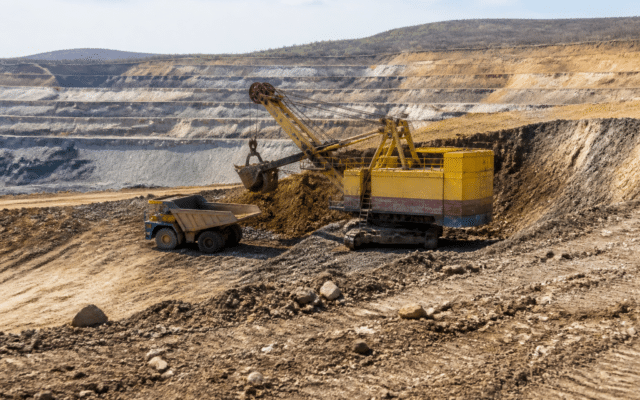 O carieră minieră în trepte, cu un excavator industrial galben de mari dimensiuni care încarcă pământ într-un autocamion de tip dumper