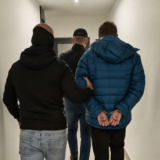 Rear view of a man in handcuffs being escorted by two officials in a hallway