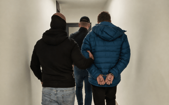 Rear view of a man in handcuffs being escorted by two officials in a hallway