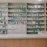 Interiorul unei farmacii cu rafturi albe pline cu diverse cutii de medicamente de diferite culori și dimensiuni