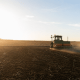 A tractor working in a vast agricultural field during sunset, illustrating farming and agricultural projects