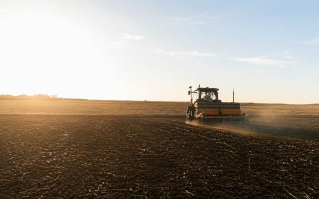 A tractor working in a vast agricultural field during sunset, illustrating farming and agricultural projects