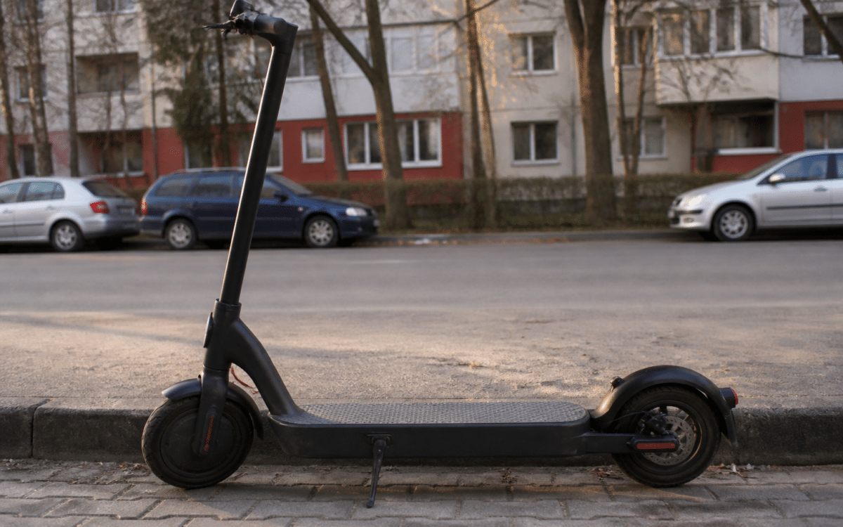 O trotinetă electrică neagră parcată pe trotuar, lângă bordura unei străzi