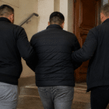 Trei bărbați văzuți din spate, urcând niște trepte spre o ușă de lemn