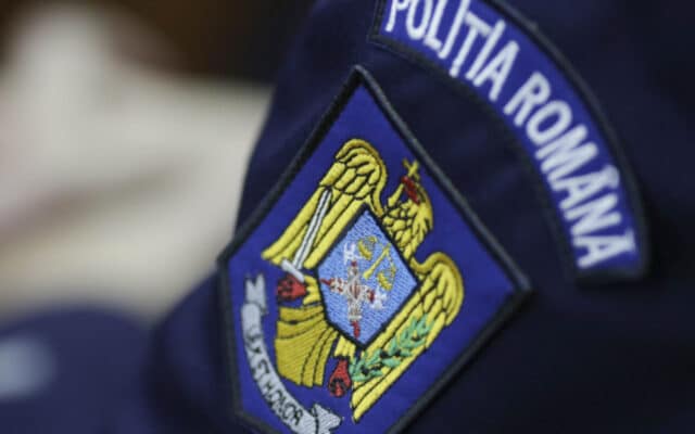 Detaliu al uniformei unui polițist, concentrat pe emblema brodată de pe braț care reprezintă stema României și inscripția instituției